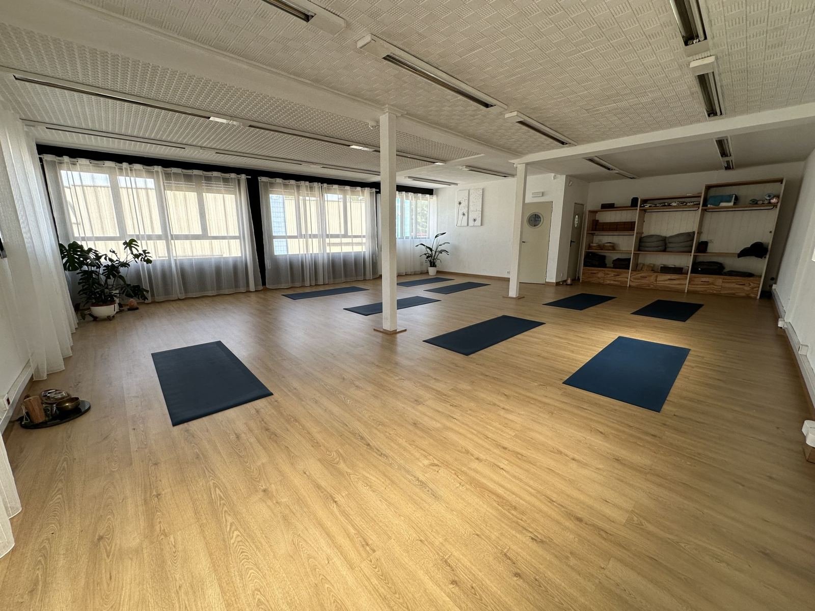 Vista general de la sala: suelo de madera, cortinas blancas y esterillas azules